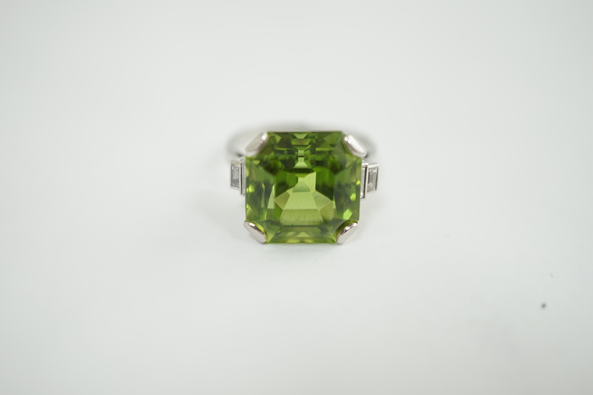 A 1920's platinum and single stone asscher cut peridot set dress ring, with four stone graduated baguette cut diamond set shoulders